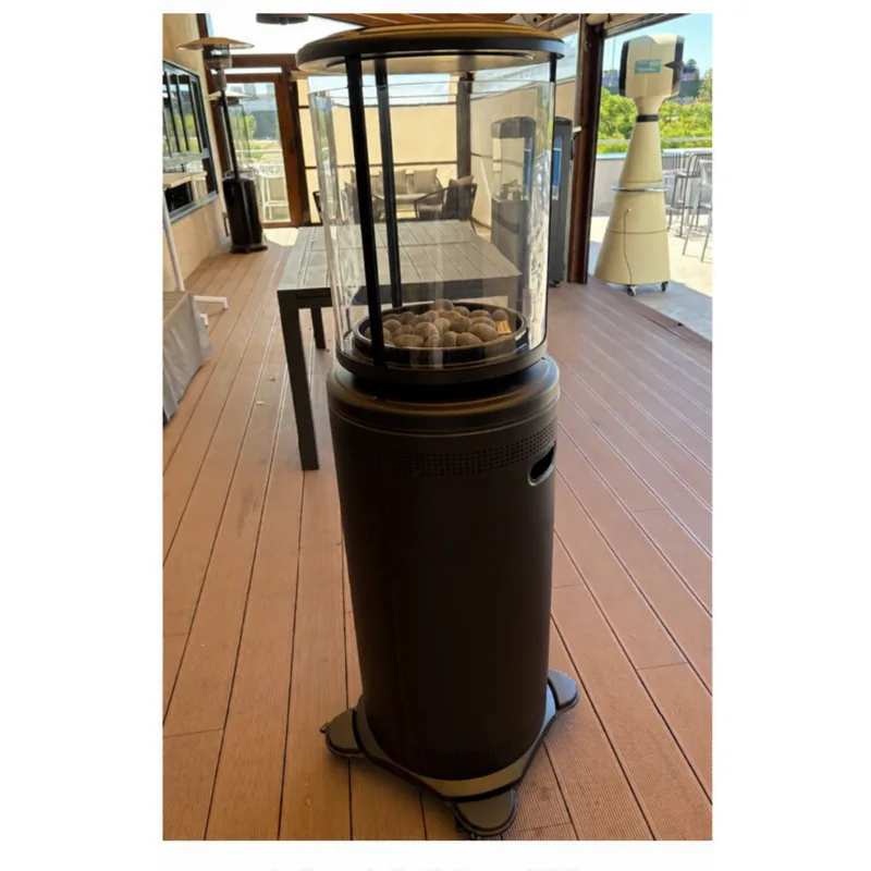 estufa a gas SAMOA REDONDA: Estufa negra de base cilíndrica con cámara acristalada circular sobre una terraza.